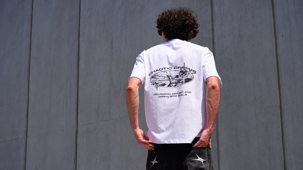 Model from behind in the Chaotic Dreams tee against a concrete wall
